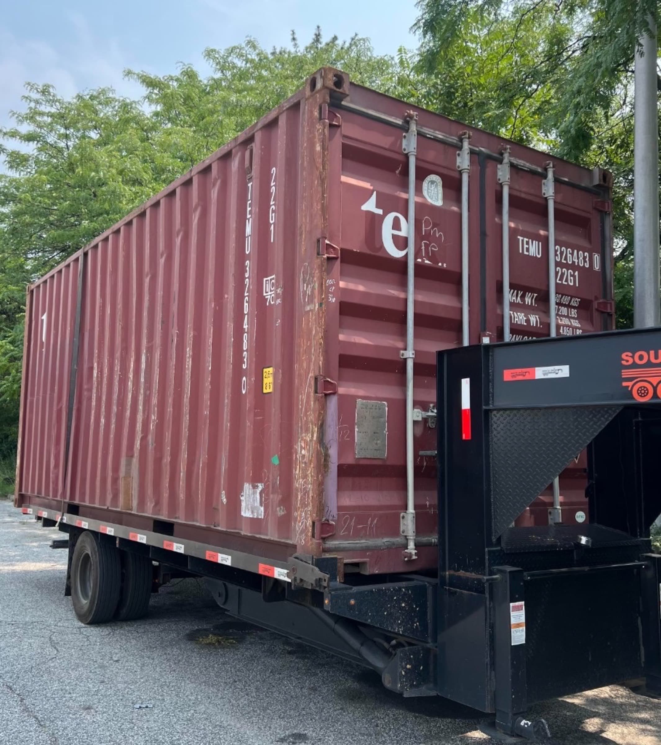 Used 20ft shipping container on a gooseneck trailer, oxide red with surface rust and depot markings