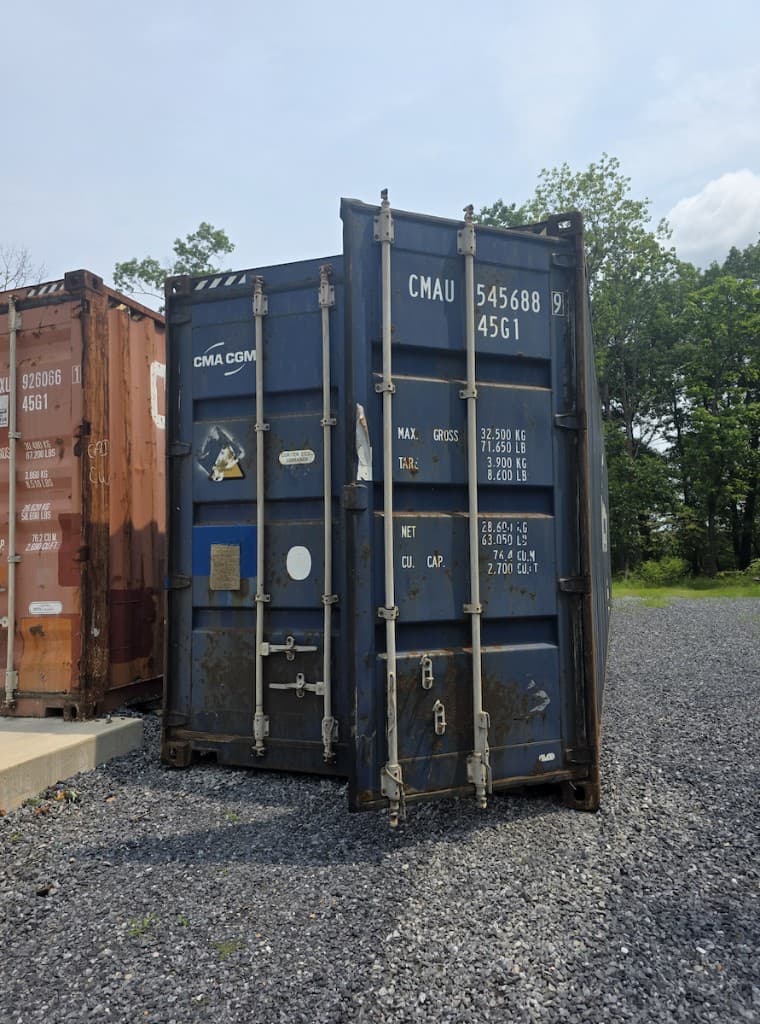 Rear doors of a used blue CMA CGM 40ft container on gravel, with surface rust on locking bars and the bottom rail