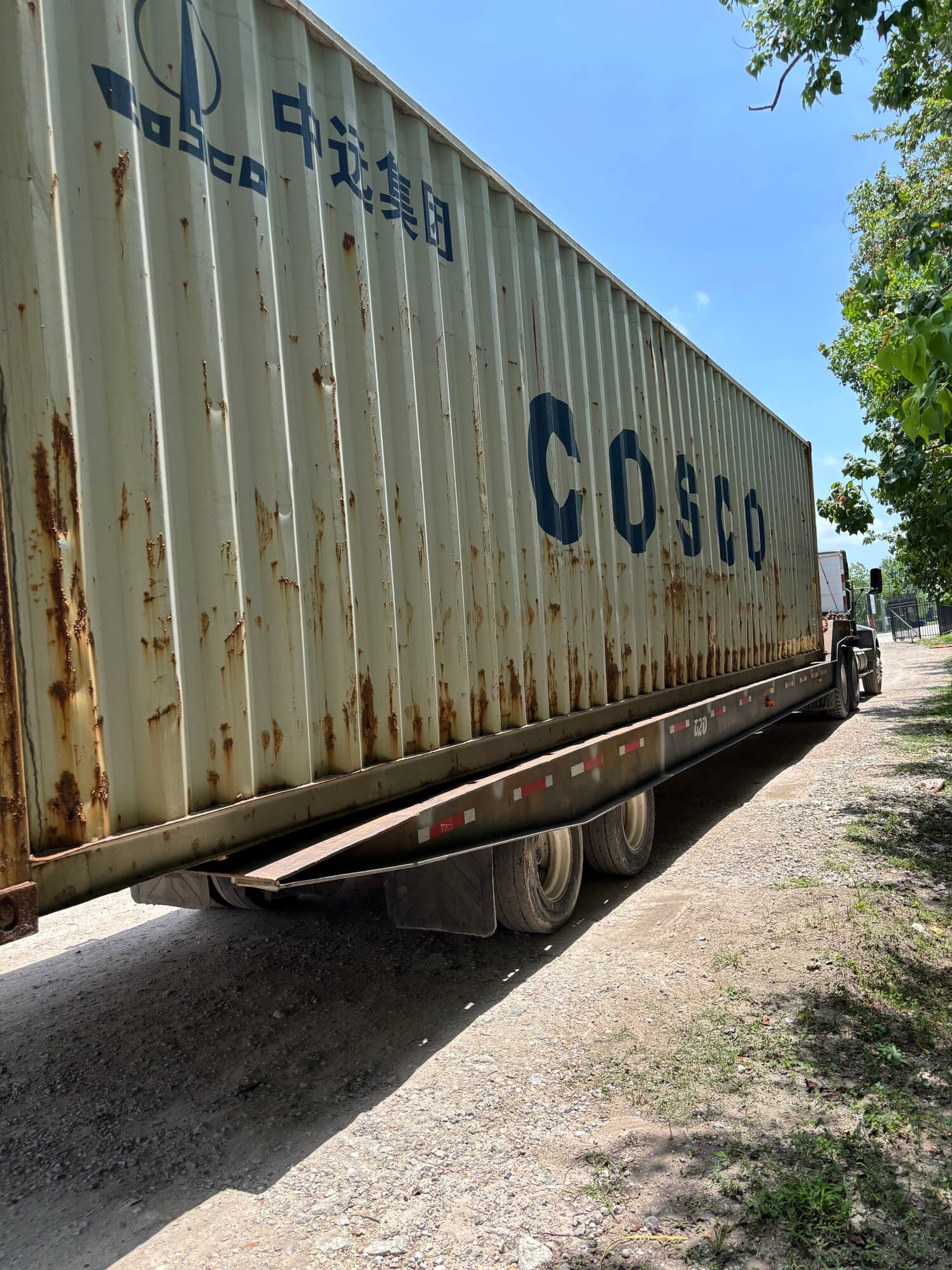 Angled side view of a used off-white COSCO 40ft high-cube container with surface rust on a trailer