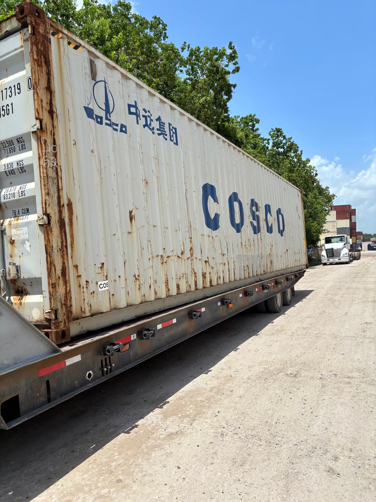 Side of a used white COSCO 40ft high-cube container on a flatbed with rust streaks and faded paint