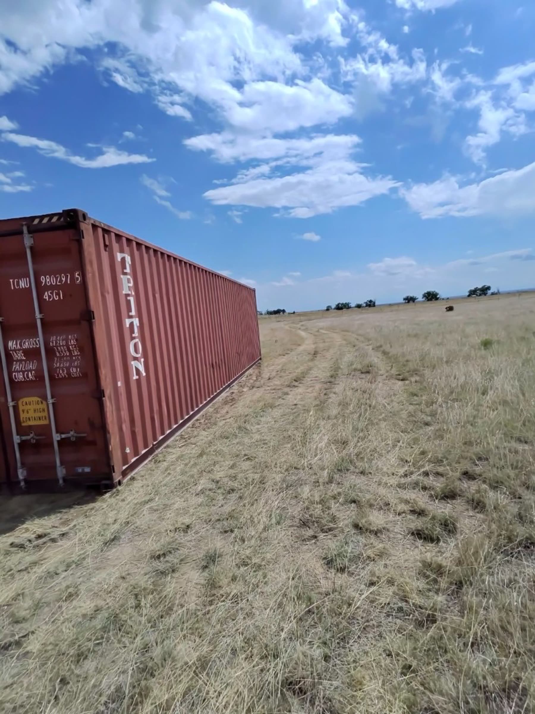 Used 40ft high-cube Triton shipping container sitting in a grassy field after delivery