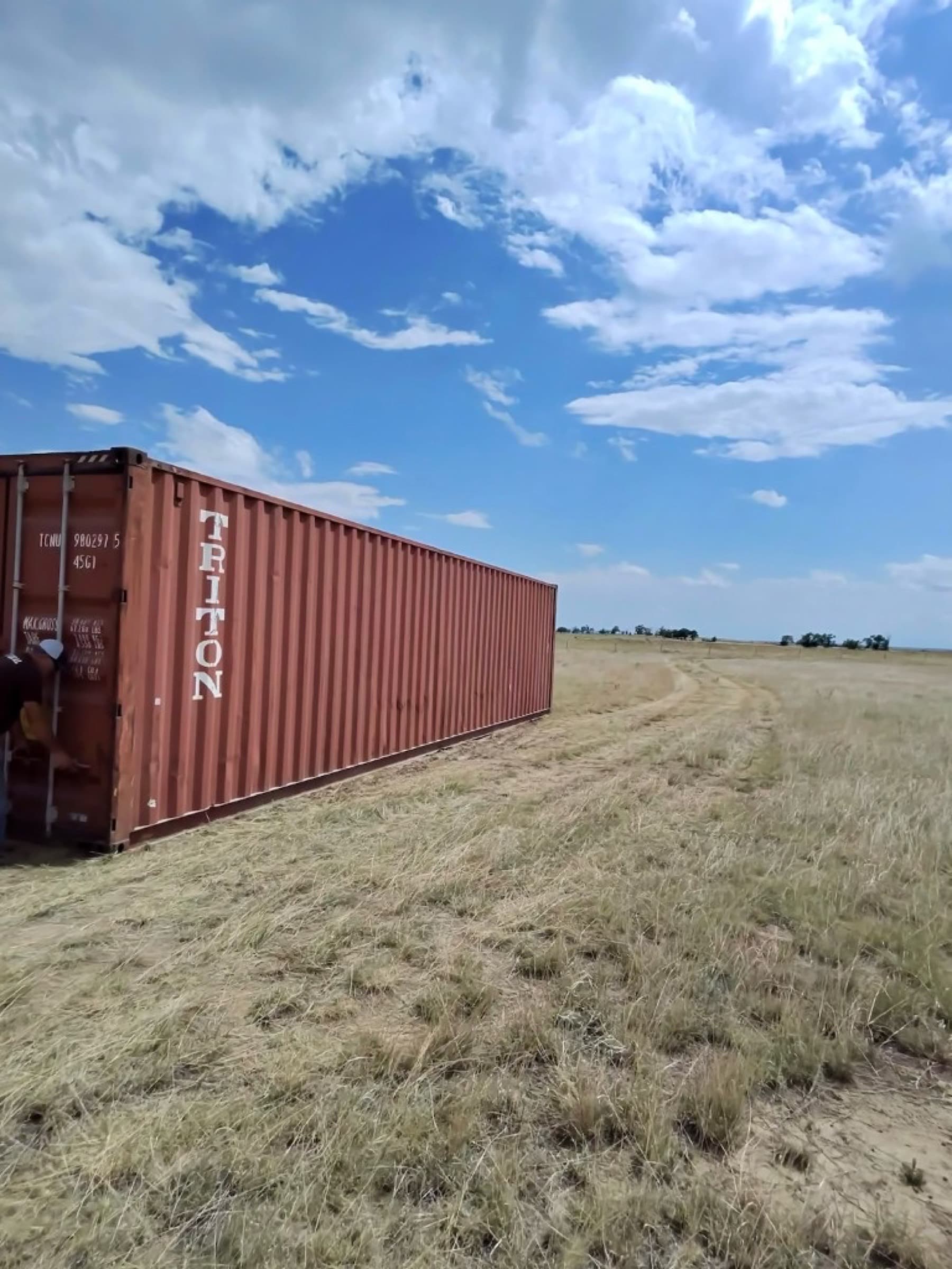 Side view of a used 40ft high-cube container in a field with a person checking the cargo doors
