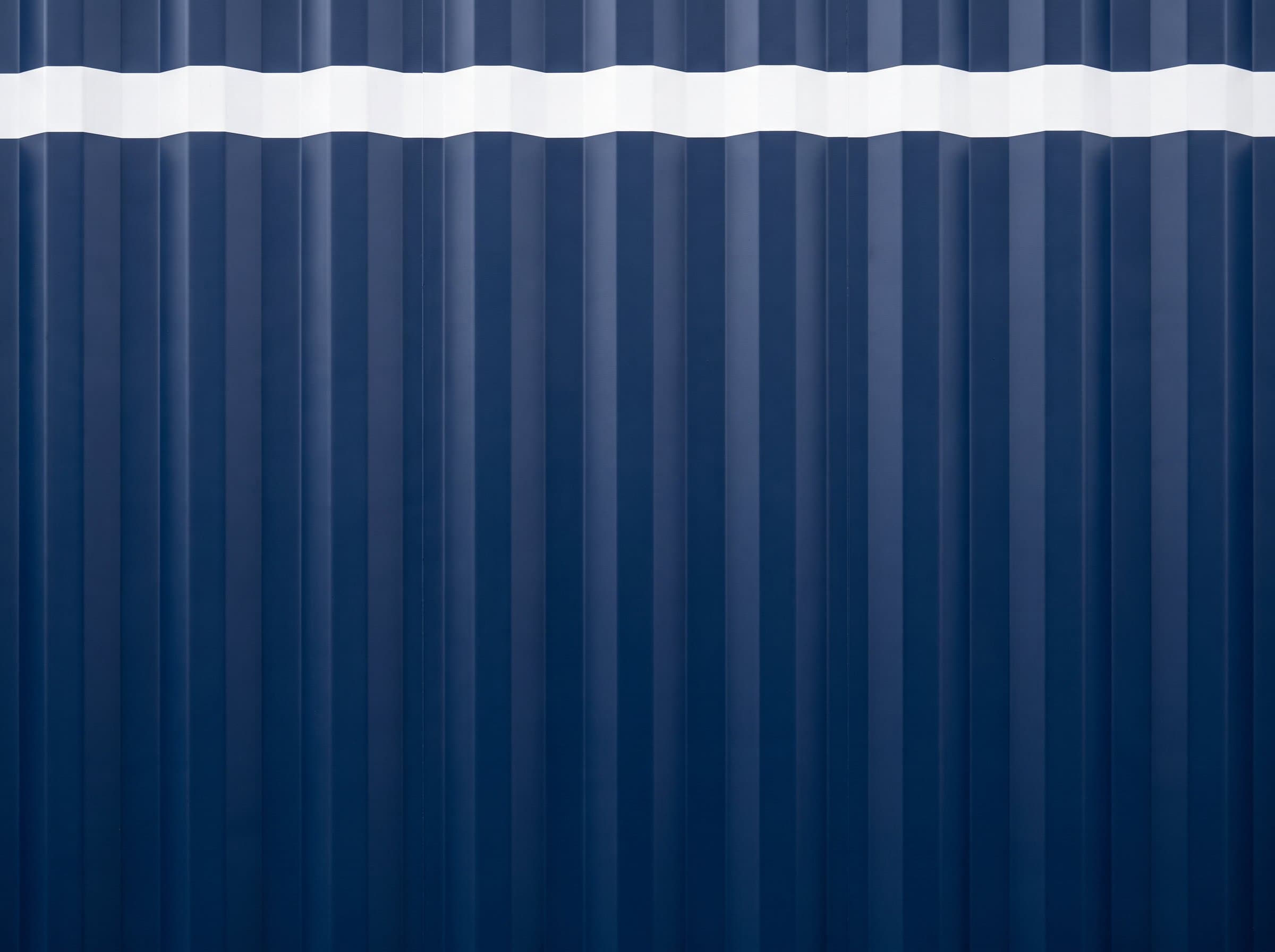 Macro detail of pristine factory-painted corrugated steel on a navy blue 40ft high-cube new one-trip container with white HC stripe
